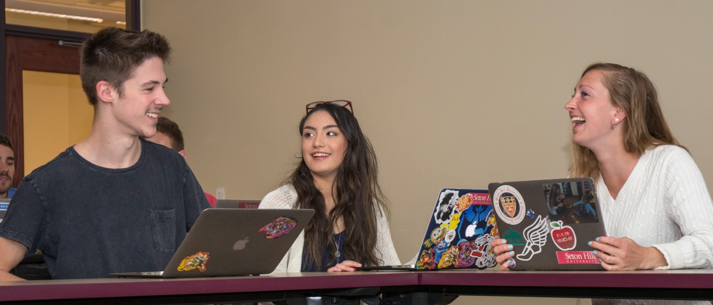 Three Seton Hill students on their laptops in a classroom