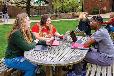 Students at a picnic table working on Macbooks