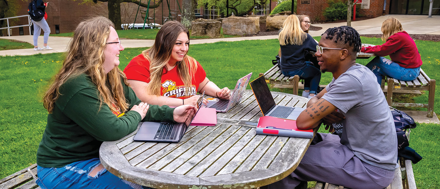 Students at a picnic table working on Macbooks